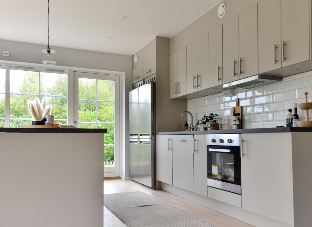 Minimalist white furniture and modern stainless steel appliances in stylish kitchen at home on sunny day